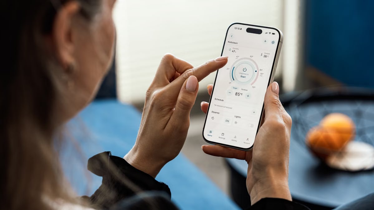 A woman uses a smartphone app to adjust her sauna settings indoors.
